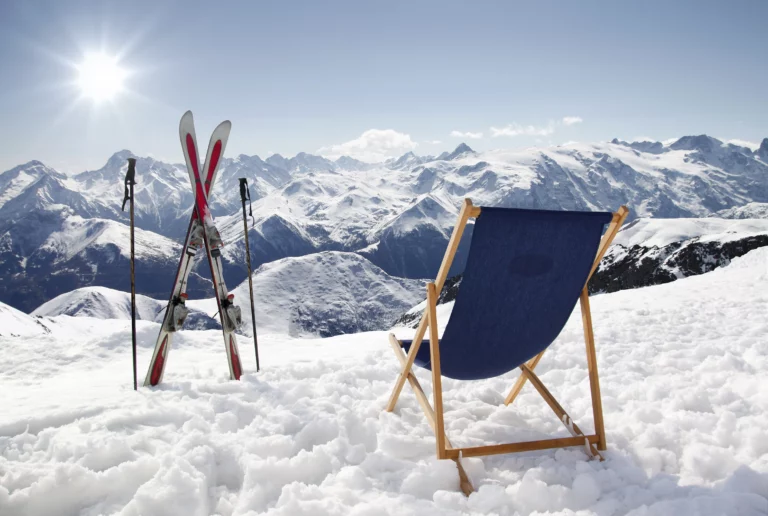 A folding chair in the snow, skis next to it